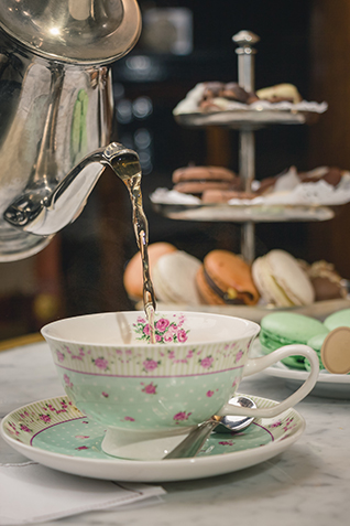 A vertical shot of a pouring tea in a cup on a marble table with desserts